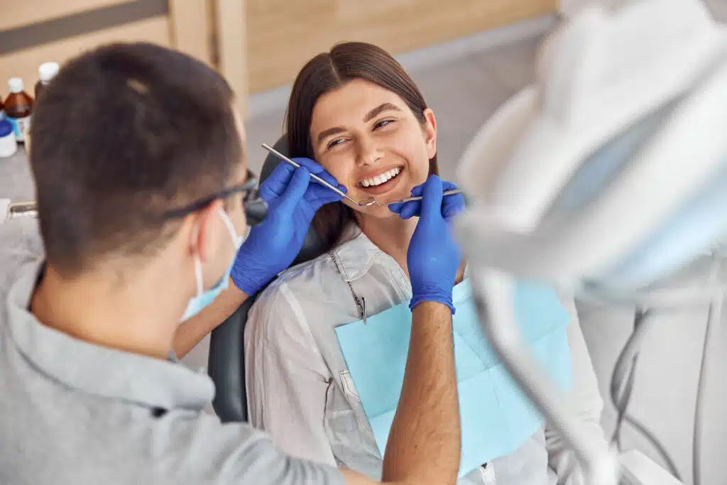 Cheerful positive dentist and client in dentistry. They look at each other and smile. Female client sit in chair